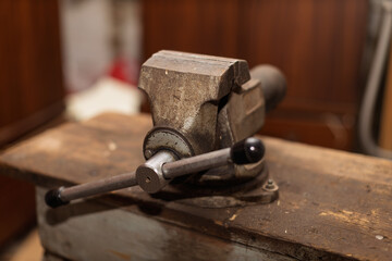A sturdy, aged metal bench vise is securely mounted on a rustic wooden workbench in a workshop.