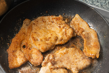 Golden-brown breaded meat is being pan-fried in a dark skillet with oil.