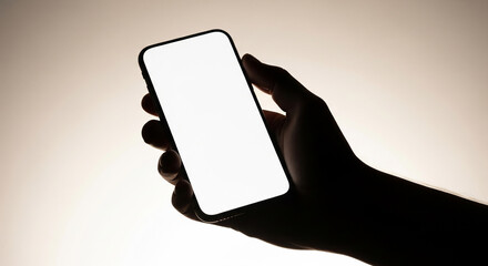 Silhouette of a hand holding a smartphone with a blank white screen. Mockup for an app or website design with dramatic backlighting and copy space for text.