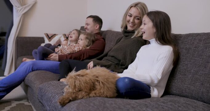 Happy family at home sitting on the sofa with the dog and watching tv