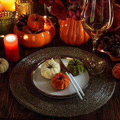 Thanksgiving table setting with decorative pumpkins, candles and string lights on dark wooden table