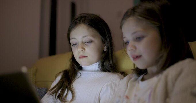 Two happy girls using digital tablet at home to read ebook and remote learning