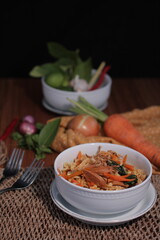 A bowl of stir-fried noodles with vegetables and tofu, garnished with herbs.