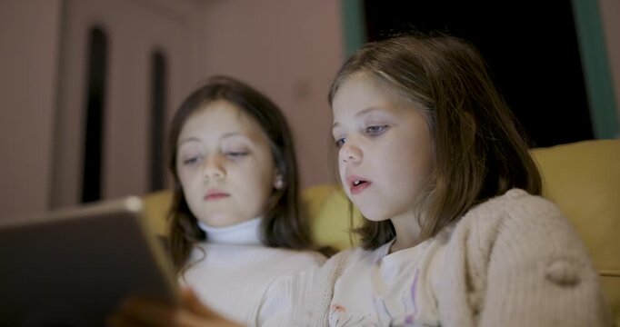 Two happy girls using digital tablet at home to read ebook and remote learning
