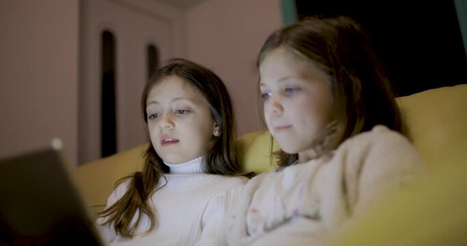 Two happy girls using digital tablet at home to read ebook and remote learning