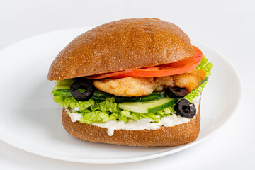 Crispy chicken sandwich topped with fresh lettuce, tomatoes, and olives on a plate