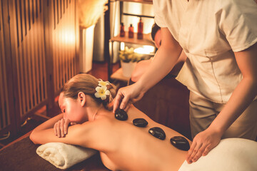 Hot stone massage at spa salon in luxury resort with warm candle light, blissful woman customer...