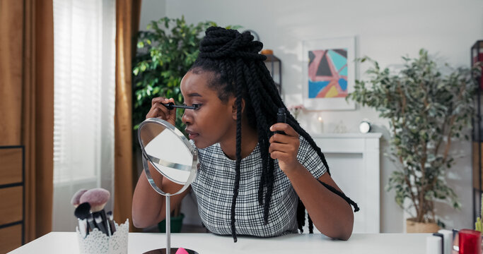 A beauty vlogger focuses on her lashes while applying mascara. Sitting at her desk, she films a video for her beauty channel, highlighting mascara benefits for everyday makeup.