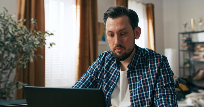 A focused person with a disability is captured in a close-up while working remotely. He sits at home, typing on the keyboard and looking at the monitor with determination.