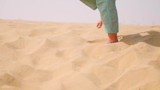 Closeup shot of feet of Indian woman walks on Thar desert at Jaisalmer, Rajasthan, India. Woman barefoot walking on sand dune. Tourist exploring desert landscape in Rajasthan.