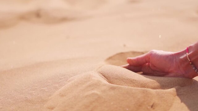 Close-up of Indian female hand releasing dropping sand in desert at Jaisalmer, Rajasthan, India. A girl holds hot sand in her hand. The concept of quickly passing time.
