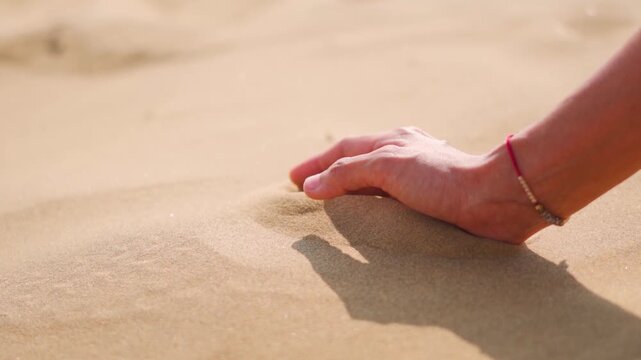 Close-up of Indian female hand releasing dropping sand in desert at Jaisalmer, Rajasthan, India. A girl holds hot sand in her hand. The concept of quickly passing time.
