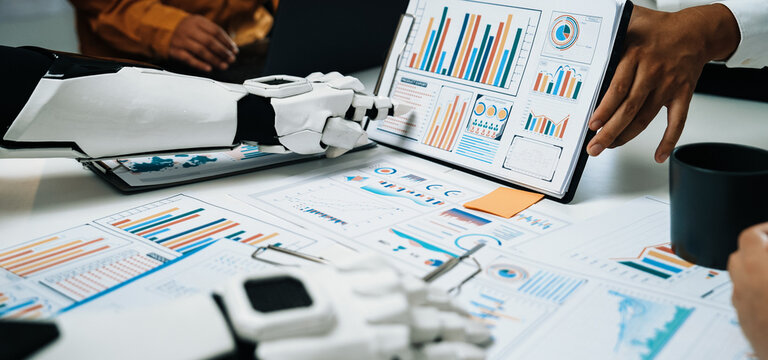 A robot and human engaging in a business meeting, showcasing charts and data analysis on a conference table, demonstrating advanced collaboration and technology in the workplace.Noogenesis