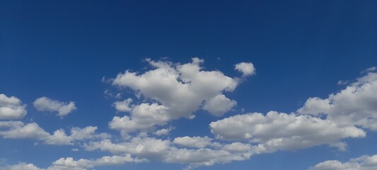 Partly cloudy cumulus clouds wander across the clear blue sky