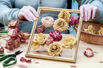Florist at work: woman shows how to transform old picture frame into a 3D composition with dried roses of different sizes. Step by step, tutorial.