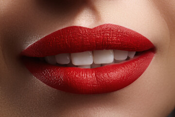 Obraz premium Macro shot of glossy matte red lips parted to show white teeth. Studio-lit close-up emphasizing lip stick texture, shine and color contrast. Ideal for beauty, cosmetology and fashion campaigns