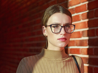 Young businesswoman wearing glasses looks confidently against brick wall in a building