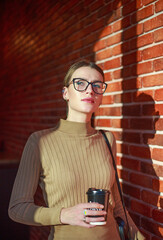 Young businesswoman wearing glasses looks confidently against brick wall in a building