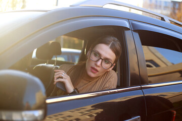 Young, confident businesswoman wearing glasses looks out of car window with excitement