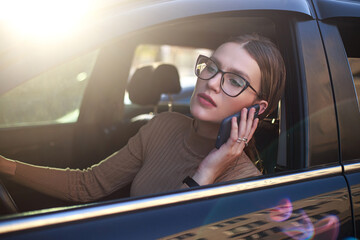 Young, confident businesswoman wearing glasses looks out of car window with excitement