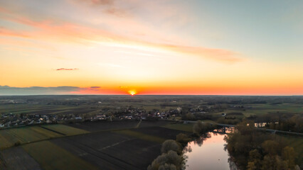 A stunning sunset over a rural landscape with fields and a winding river. The sky displays vibrant colors, creating a serene atmosphere in the countryside.