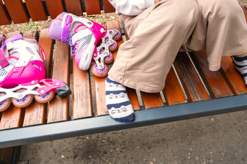 Child sits on a wooden bench wearing playful socks next to bright pink roller skates. The vibrant colors suggest a playful moment of rest after skating outdoors.