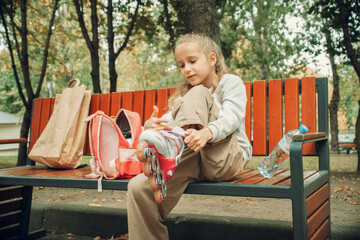 Child Putting on Roller Skates with Backpack in Park