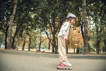 Young child rollerblading through a tree-lined park wearing a helmet for safety. The setting is serene, with benches and scattered leaves, capturing an active, joyful moment.