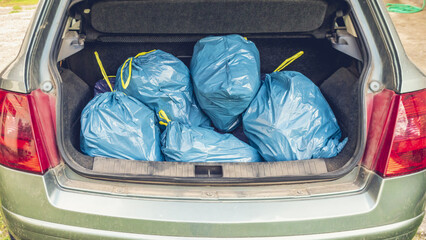 Several blue plastic garbage bags filled and placed inside a car trunk, symbolizing waste disposal, cleanup, recycling, and environmental responsibility. © NewPixelWave
