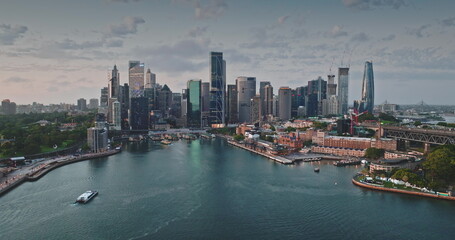 Obraz premium Australia, Sydney: Breathtaking aerial view of Sydney modern skyline city center reflecting in calm harbor waters. Iconic skyscrapers cityscape illuminated by soft sunset light. Drone panorama