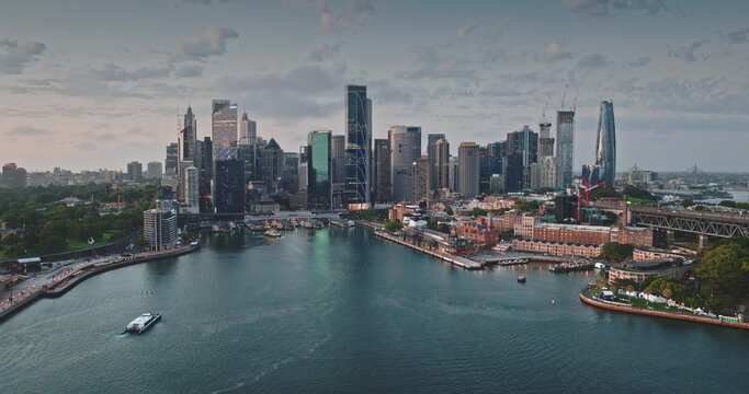Australia, Sydney: Breathtaking aerial view of Sydney modern skyline city center reflecting in calm harbor waters. Iconic skyscrapers cityscape illuminated by soft sunset light. Drone panorama