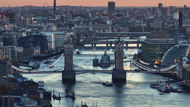 Aerial view of Tower Bridge and HMS Belfast warship on River Thames at sunset, with London skyline cityscape in background, offering a captivating urban landscape. Travel to UK. Drone flight
