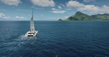 Fototapete Segeln Fiji, Kuata island: White catamaran with tourists sailing blue ocean water near tropical island, under bright sunny sky. Remote wild nature paradise, exotic summer travel. Aerial drone flight  © Goinyk