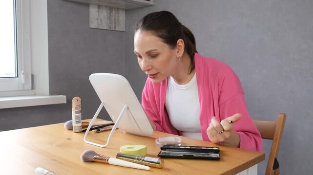 A woman applying makeup at a mirror vanity table