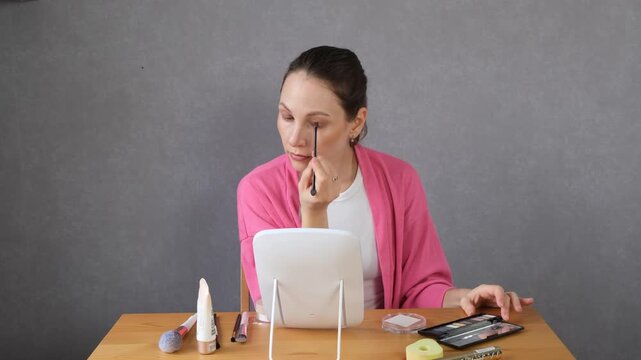 A woman applying makeup at a mirror vanity table