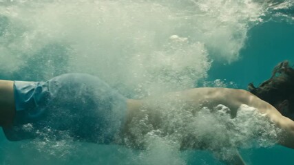 A man dives headfirst into clear blue water, swimming gracefully below.