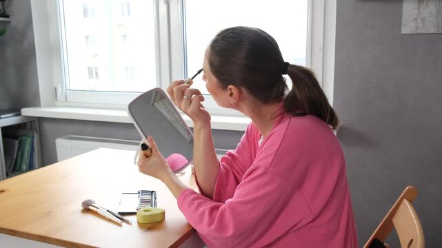 A woman applying makeup at a mirror vanity table