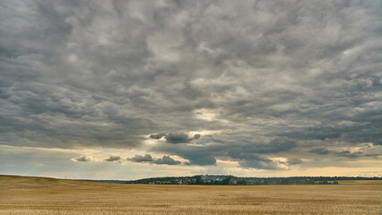 clouds over an agricultural field. A spring landscape with a forest, an empty field and clouds. A field after harvesting wheat.