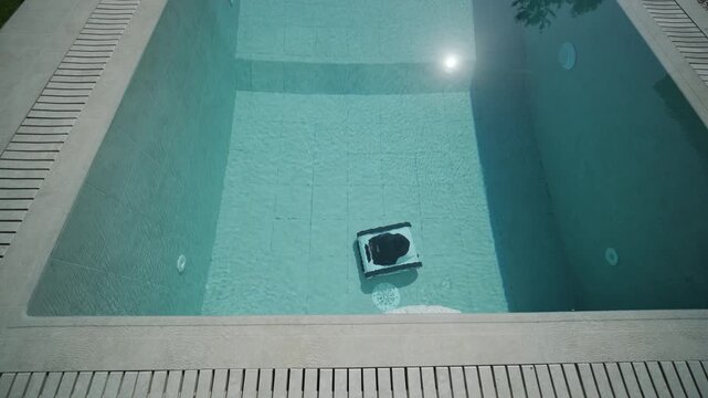 Robotic pool cleaner moving along the edge of a clear blue swimming pool