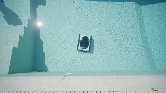 Robotic pool cleaner moving along the edge of a clear blue swimming pool