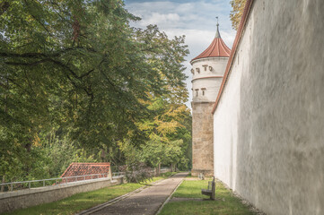 Runder historischer Turm Feilturm an umlaufender Stadtmauer mit überdachtem Wehrgang an Reimlinger Mauer, Mauerpartie mit gepflegter Parkanlage in Nördlingen  vor blauem Himmel mit Wolken