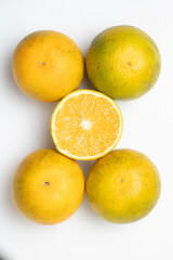 Cinco naranjas criollas en fondo blanco con la mitad de una de ellas cortada en el centro, en ángulo cenital.