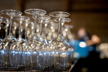 Clear wine glasses lined up for an event at a rustic venue with blurred background activity
