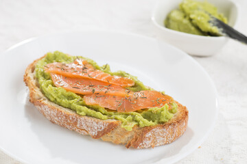 A slice of bread with avocado and salmon decorated with thyme
