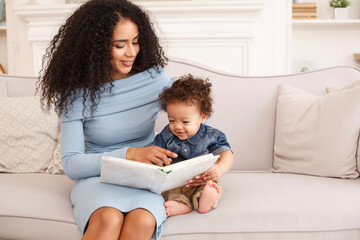 Happy mother reading a book with her little child on sofa. Family time, learning, bonding, and love...
