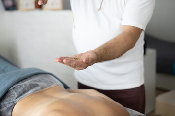 Obraz premium Close-up of a massage therapist pouring massage oil into the hand before starting a relaxing back massage session. Concept of wellness, body care, and professional spa treatment.