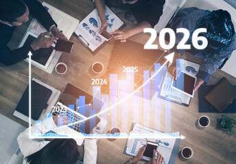 A business team collaborates in a meeting, analyzing growth projections for 2026 using graphs and charts placed on the table, highlighting strategic planning sessions. Tessel