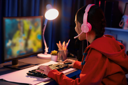 Host channel of young beautiful Asian gaming streamer playing fighting Moba at battle arena game on pc screen with multiplays, wearing pastel headphone at neon digital light modern room. Stratagem.