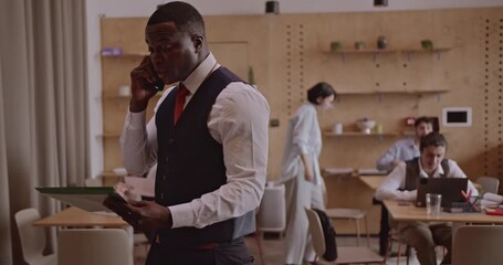 Multicultural business team discusses strategy in a modern office. A businessman talks on his phone while reviewing documents with a colleague. - Powered by Adobe