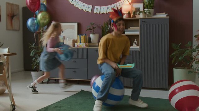 Two boys in costumes playing with toy swords, while riding bouncing balls during festive birthday celebration with other children